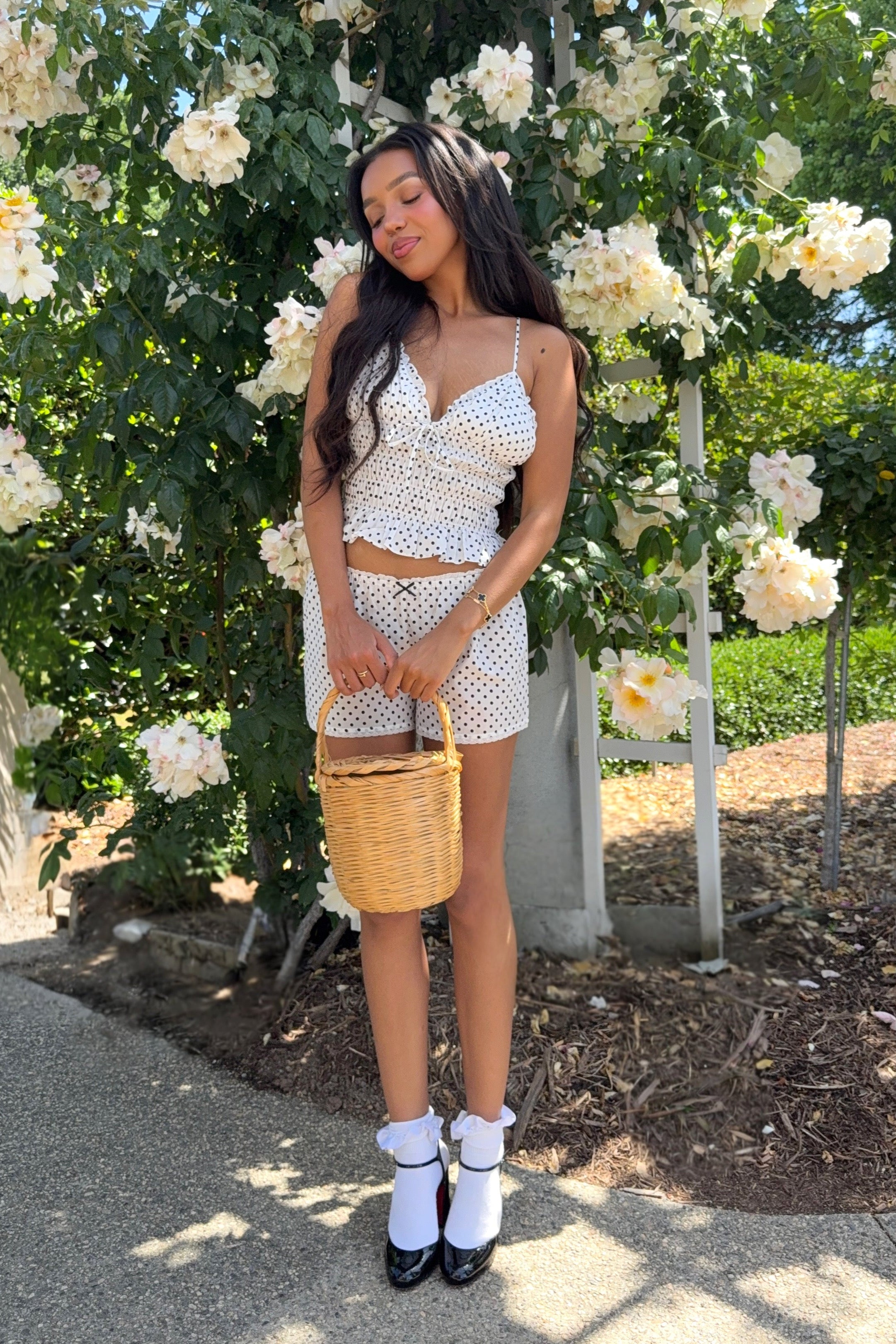 Woman in a white polka dot outfit standing in front of white flowers